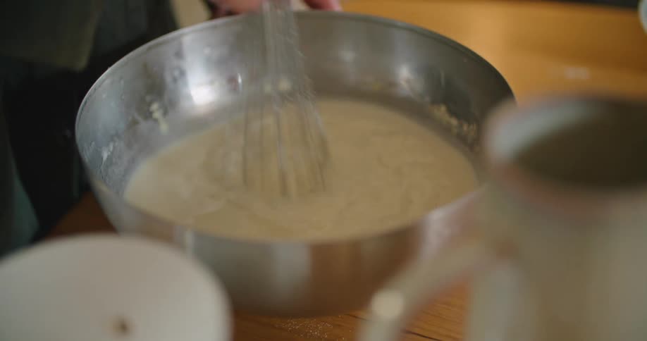 A person in the kitchen whisking batter in a mixing bowl on a table