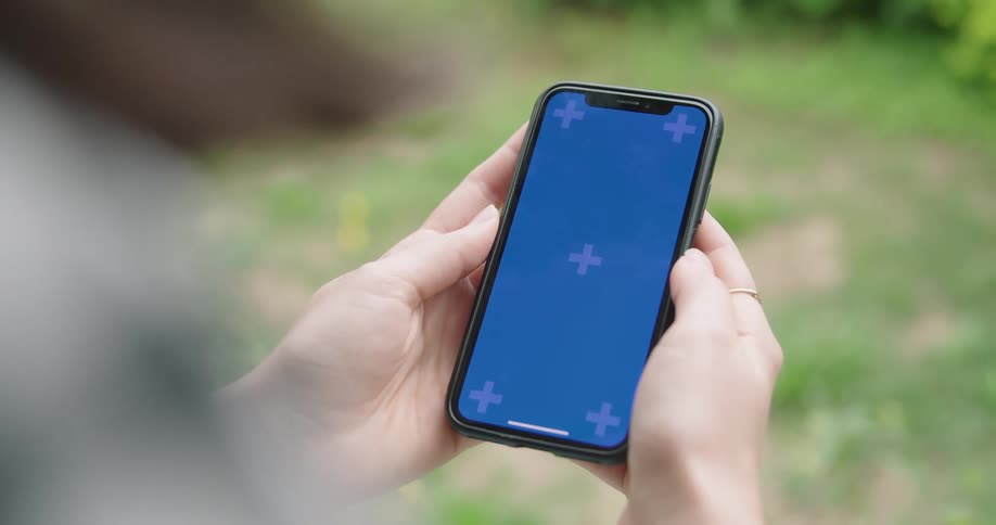 A man uses his smartphone with both hands while outside