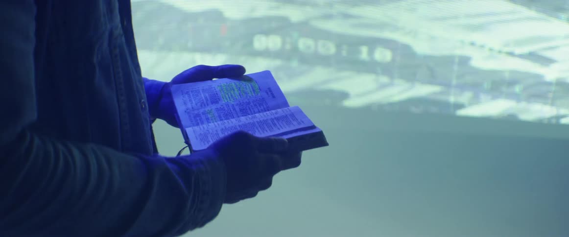 A person is holding an open book near a projector screen