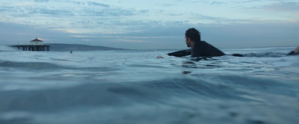 A surfer lies on his surfboard and paddles through the ocean