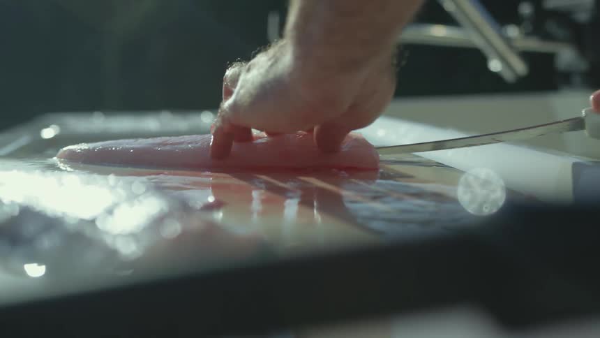 A chef uses a knife with a long thin blade to cut a piece of fish
