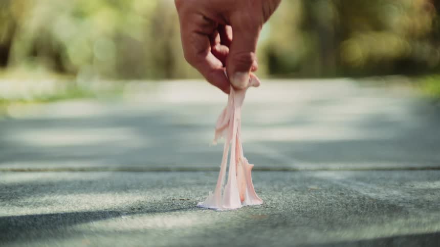 A person taking chewing gum off the road with plants and trees in the background