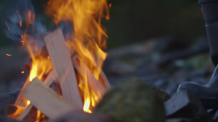 A man fueling a campfire with chopped wood at evening