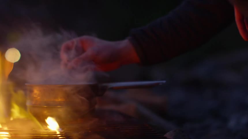 A person is stirring a pot on the grill