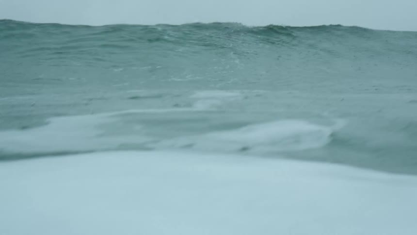 A man with a wetsuit laying on a surfboard and diving underwater with the sky and clouds in the background