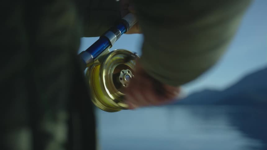A fisherman reeling in a fishing pole next to a lake