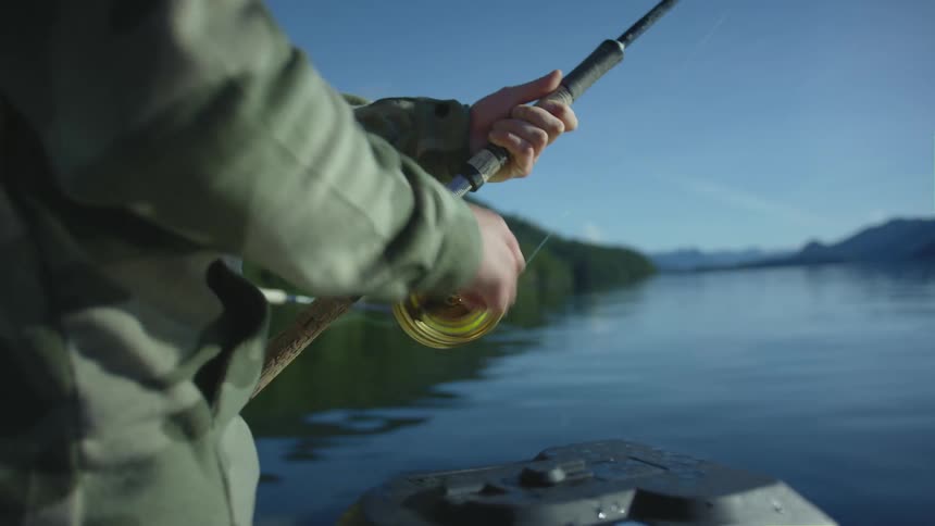 Man standing on a boat in a lake reeling a fishing line