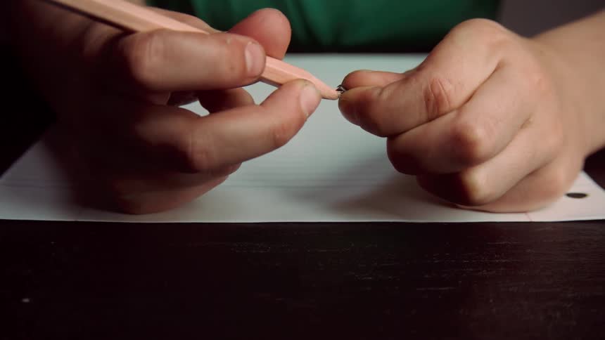 A person sitting at a table with papers trying to put a point back into a pencil