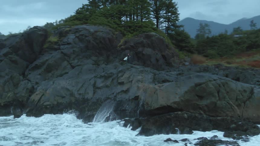 The rough waves crash against the large rocks on the shore