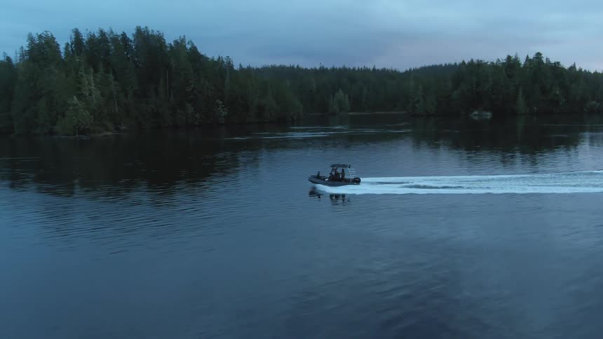 Boat travels across the lake fast close to the coast with forest at dusk