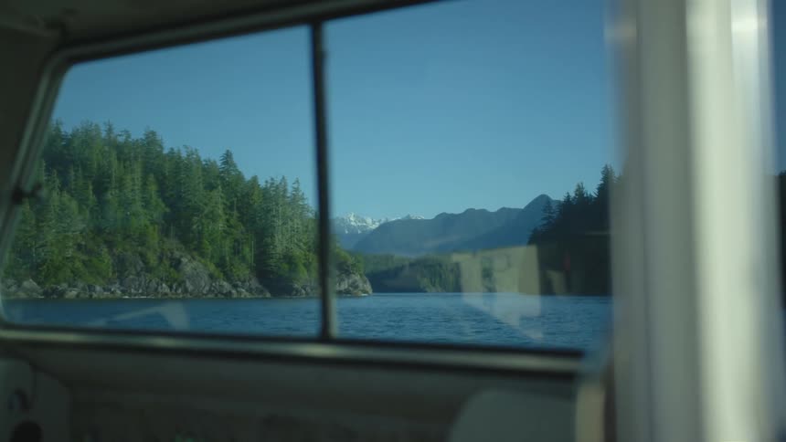 A boat with a window on a lake with trees the sky and clouds in the background