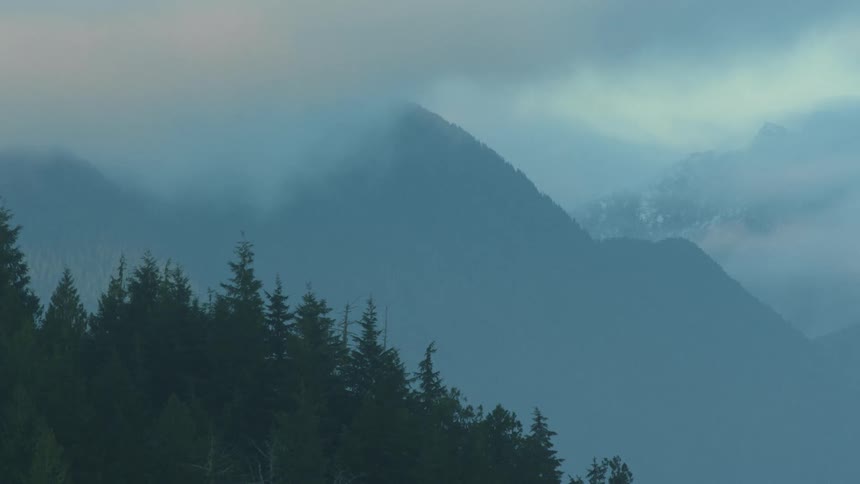 Clouds hanging over the mountain peaks close to the pine tree forest