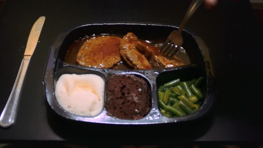 A person using a fork to spin meat in sauce on a tray on a table