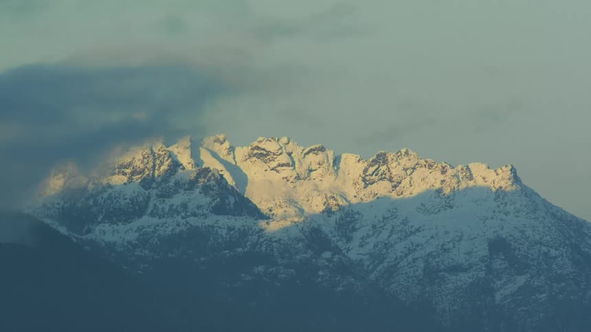 A mountain range covered with snow and ice with the sky and clouds in the background