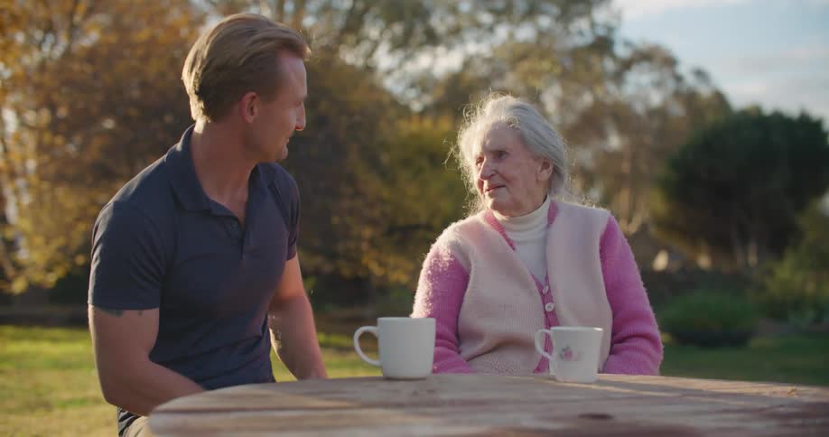 A man and woman sitting at a table with mugs with trees the sky and clouds in the background