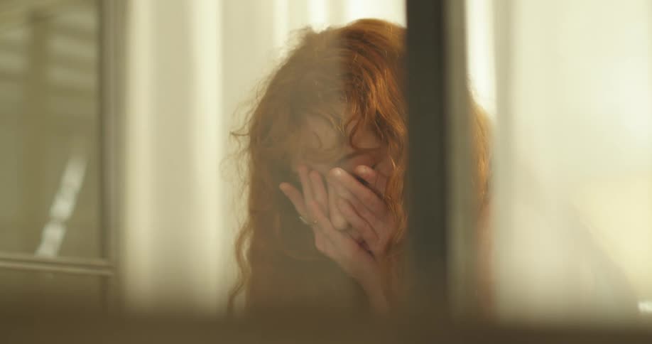 A teenage girl sits at home and puts her head in to her hands