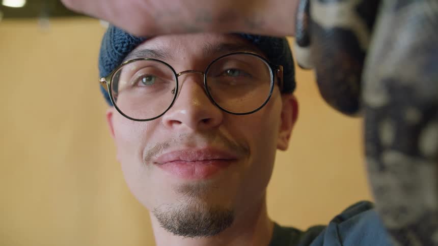 A man with a snake wrapped around his harm smiles while looking into the camera