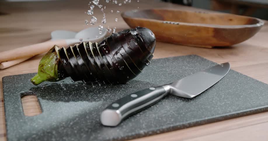 A chopped up eggplant falling on a cutting board with a knife on a table