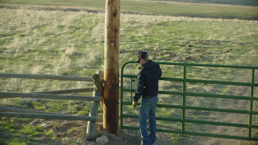 A young modern rancher closes the gate after tending to Bison in the early morning light in the Mountains of Montana
