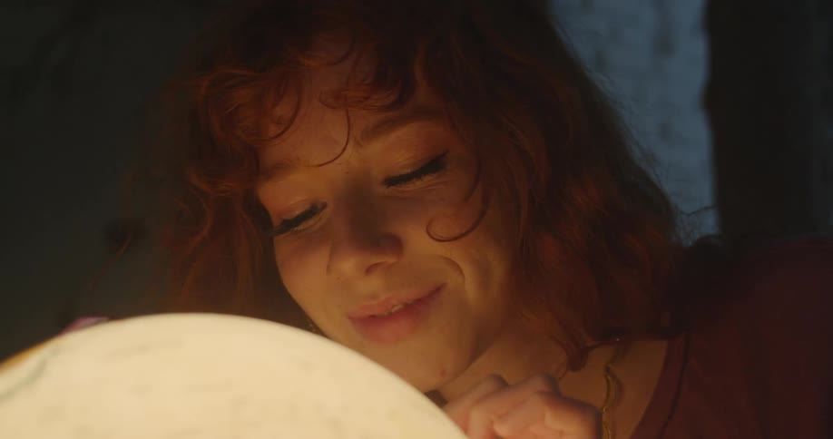 A young woman smiles while examining a glowing globe in a dimly lit room