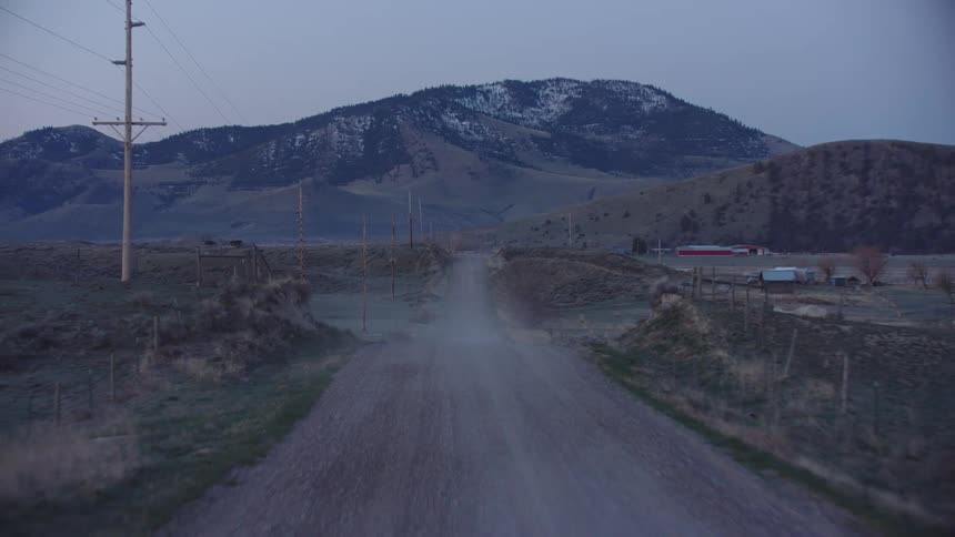 Traveling down a dirt road kicking up a lot of dust listening to country music and drinking coffee before a busy day on the ranch
