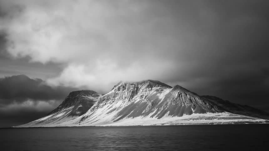 Clouds moving over a snow covered mountain and leaving a shadow on the ground