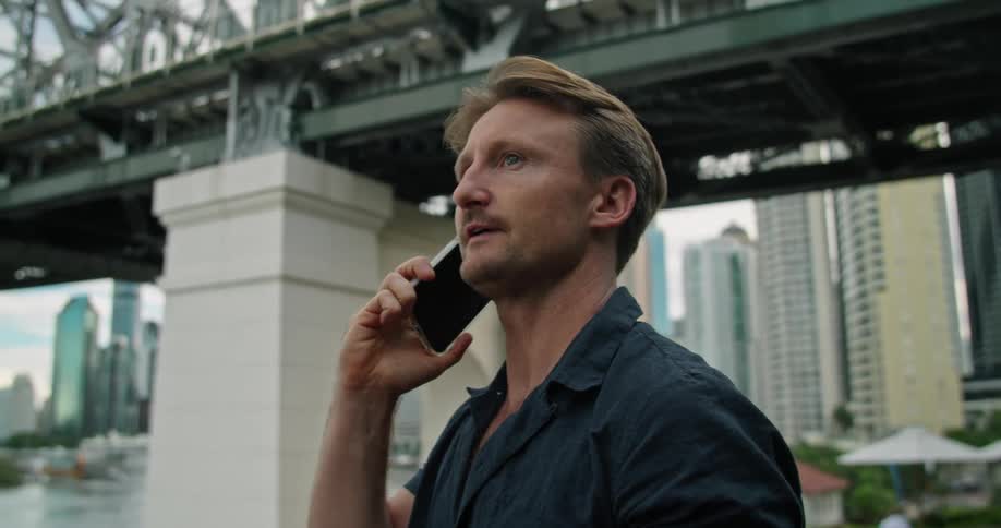 A man is talking on his cell phone by the bridge