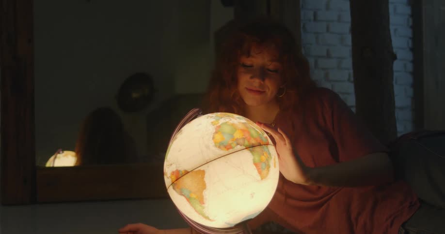Redhead girl laying on the floor looking at a glowing globe at night