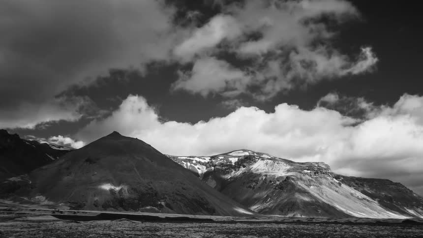 Clouds moving over snow covered mountains leave a shadow below