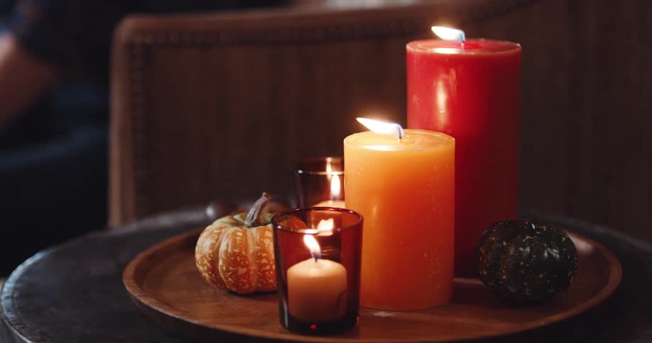 Orange and red candles burning over a tray decorated with small pumpkins