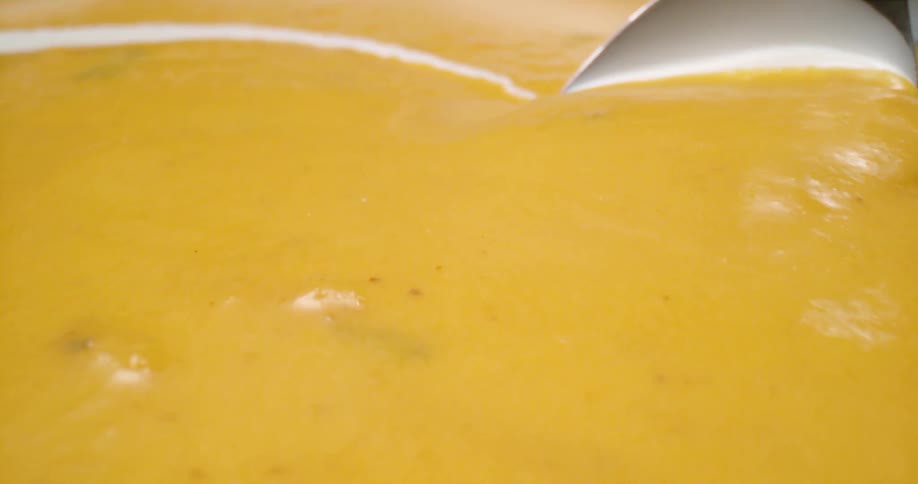A close up of a spoon being stirred in a yellow soup