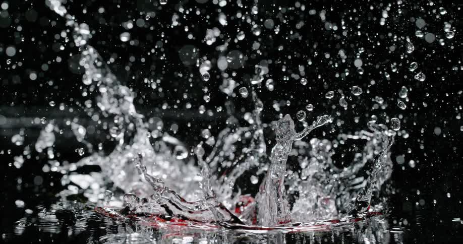 Falling red jalapeno peppers splashing water against a black background