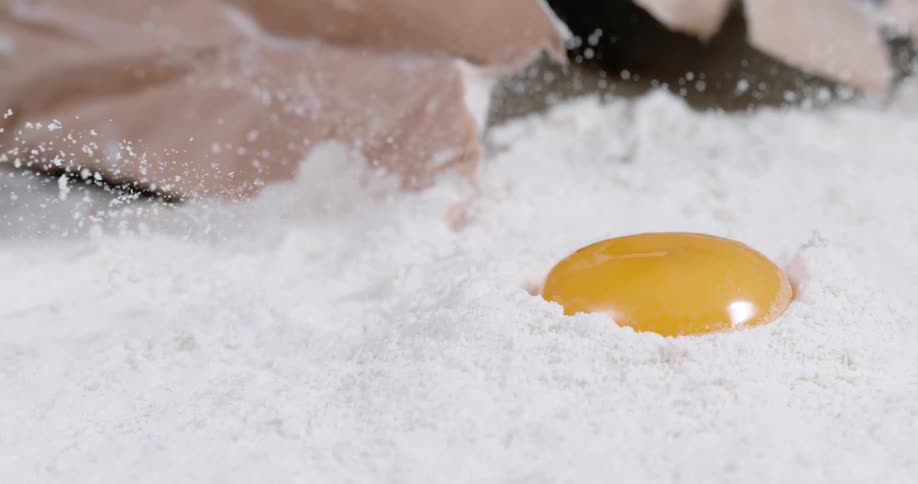 An egg yolk falling into flour on a table with a bag in the background