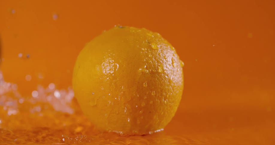 An orange in a room with water droplets falling on it and splashing