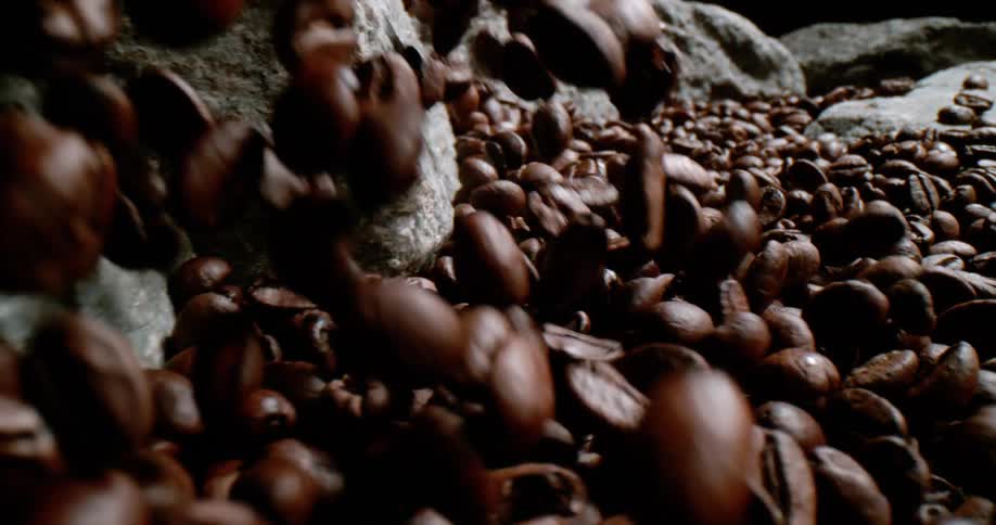 Dark roasted coffee beans falling down over rocks