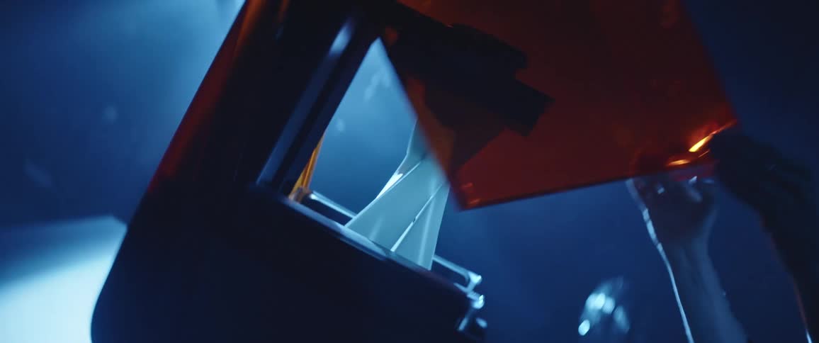 A person opens the lid of a 3d printer inside a dimly lit room