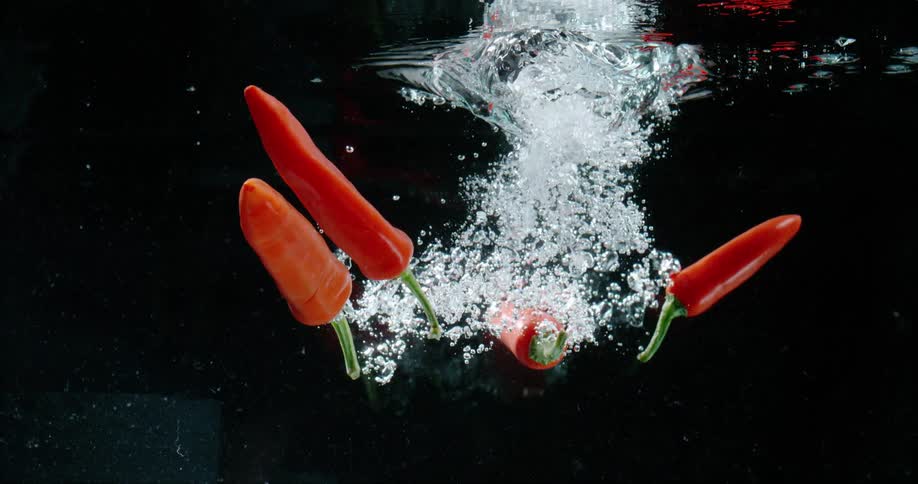 Falling red jalapenos splashing under water against a black background