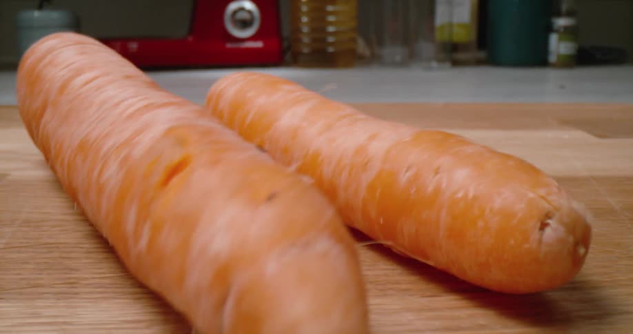Carrots rolling on a cutting board in a room with containers in the background