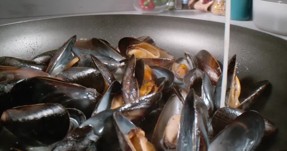 Liquid is poured on mussels in a pan to cook