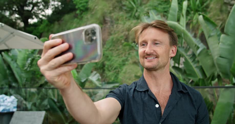 Man standing outdoors answers a video call on his phone