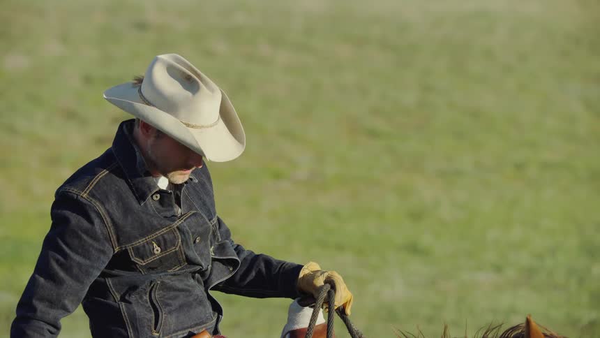 A rugged cowboy gets ready to shut down the bison ranch at sunset on horseback