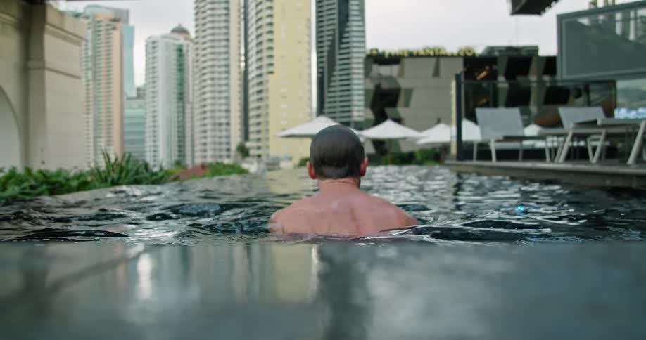 A man swimming on a rooftop pool surrounded by skyscrapers