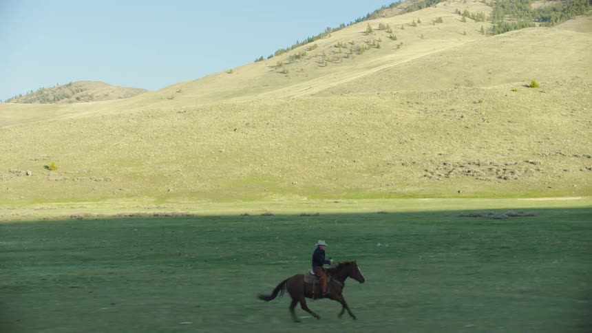 Wide shot of a cowboy galloping  in a wide mountain valley in Spring