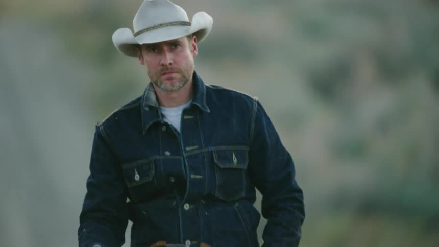 An iconic square jawed cowboy rides his horse straight towards camera after wrapping up a hard days work on a bison ranch in Montana