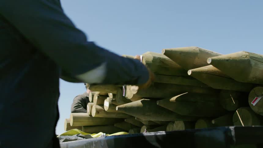 Two ranching men unload fence posts from a flatbed pickup truck on a large ranch in Montana under a Big Blue Sky