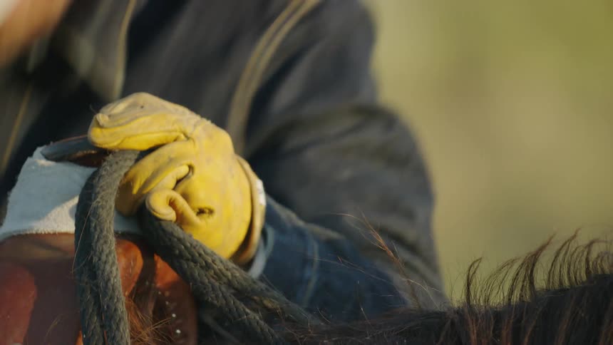 Tight shot of a cowboy getting off his horse in beautiful sunset evening light deep in Montana