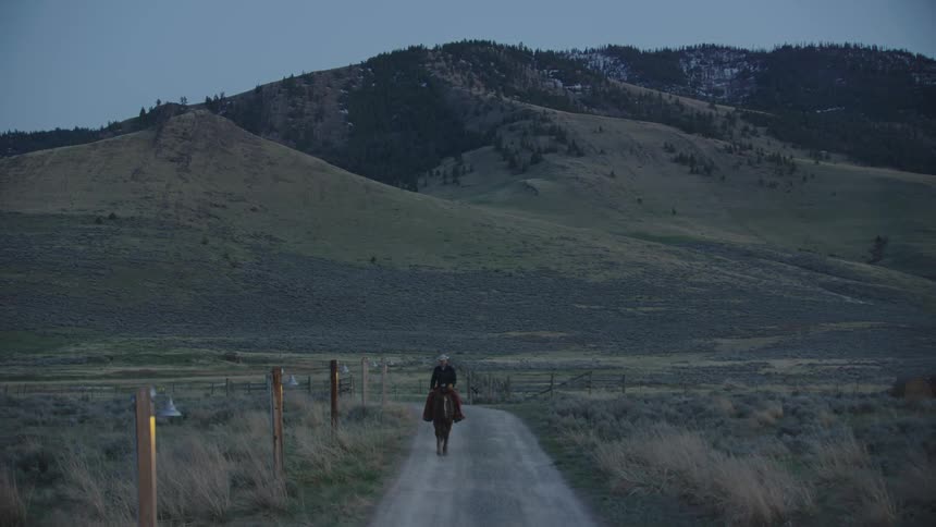 Cowboy riding a horse on a dirt road in the countryside at morning after working hard mending fence and raising bison all day long