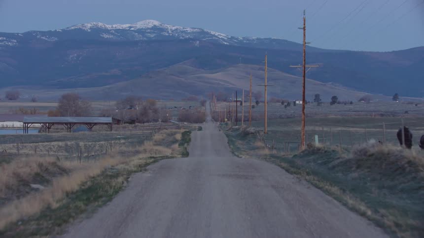Snow capped mountains and a rolling dirt road in rural Montana on another morning before the hard work begins