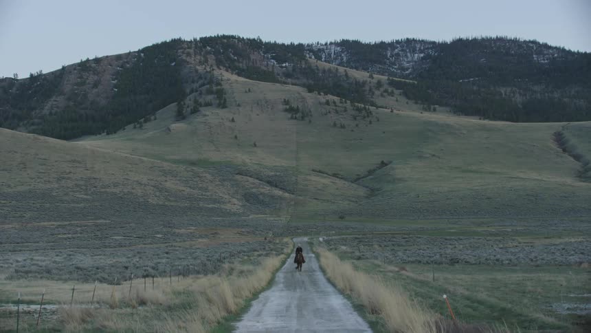 Beautiful blue hour early morning shot of a lone cowboy riding his horse directly towards camera on a straight and narrow dirt road in Big Sky Country Montana