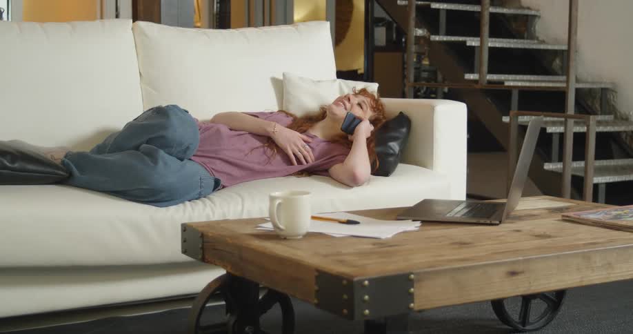 A woman lays on the couch talking on the cell phone